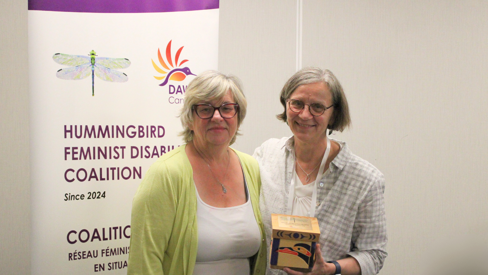 Photo of Bonnie Brayton and Deborah Stienstra posing together and holding the Hummingbird Award for the Live Work Well Research Centre