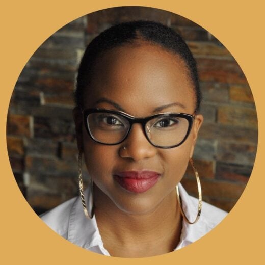 A Black woman wearing glasses, large gold hoop earrings, and a white shirt.