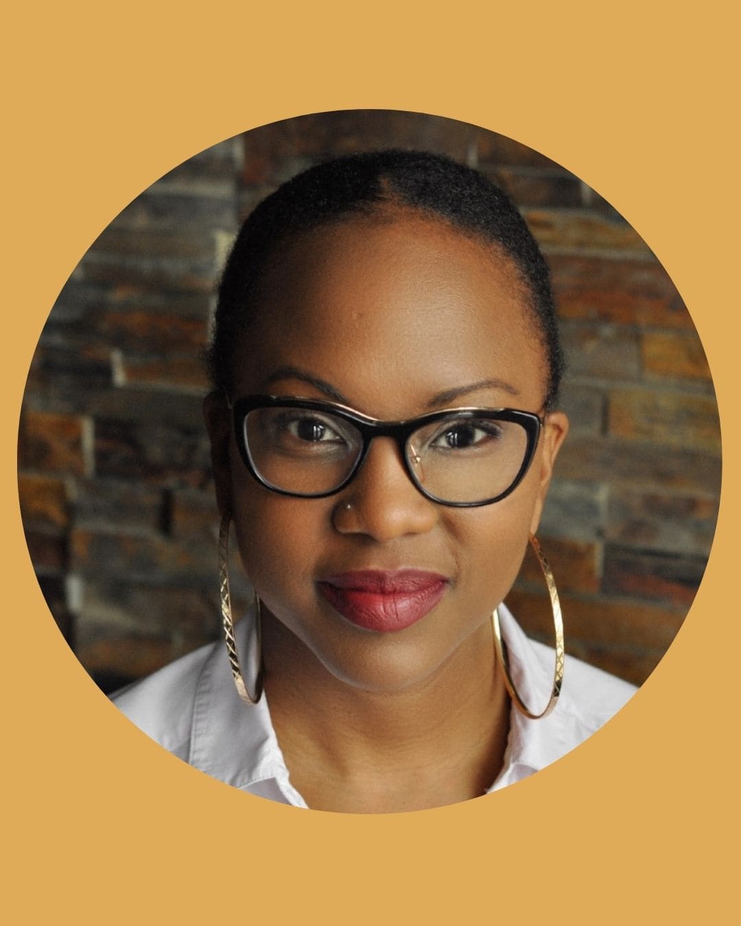 A Black woman wearing glasses, large gold hoop earrings, and a white shirt.